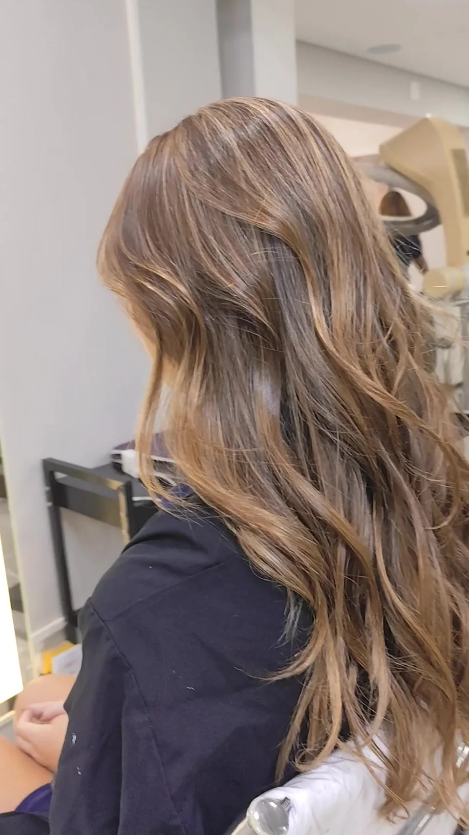 Cabelo longo com reflexos dourados e ondas, visto de costas em ângulo lateral